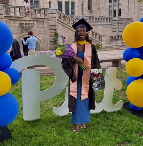 student posing in front of Pitt sign with blue and gold balloons and in front of the Cathedral of Learning