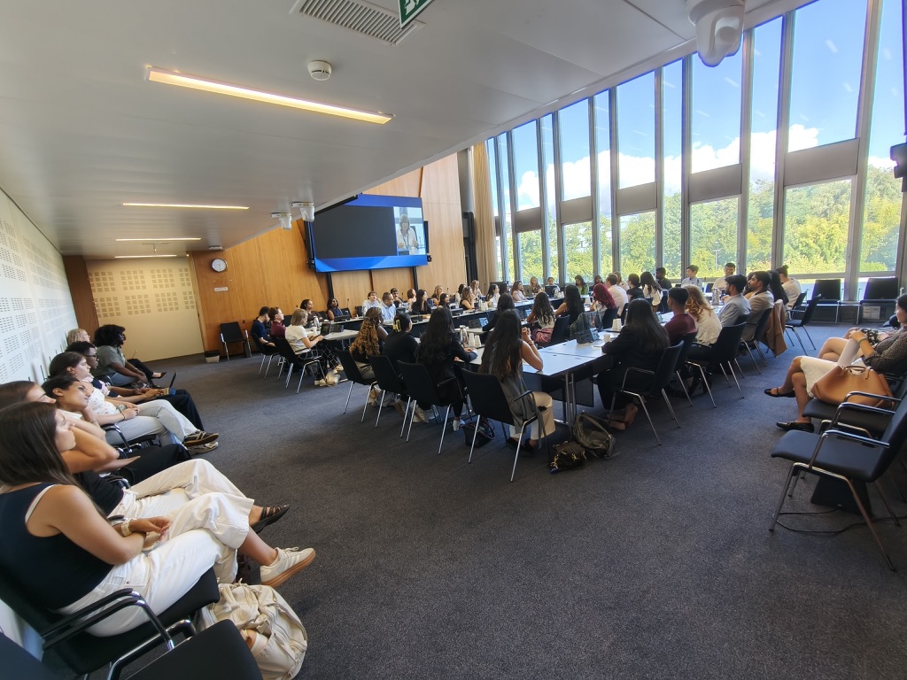 50+ people in chairs listing to someone on a screen.