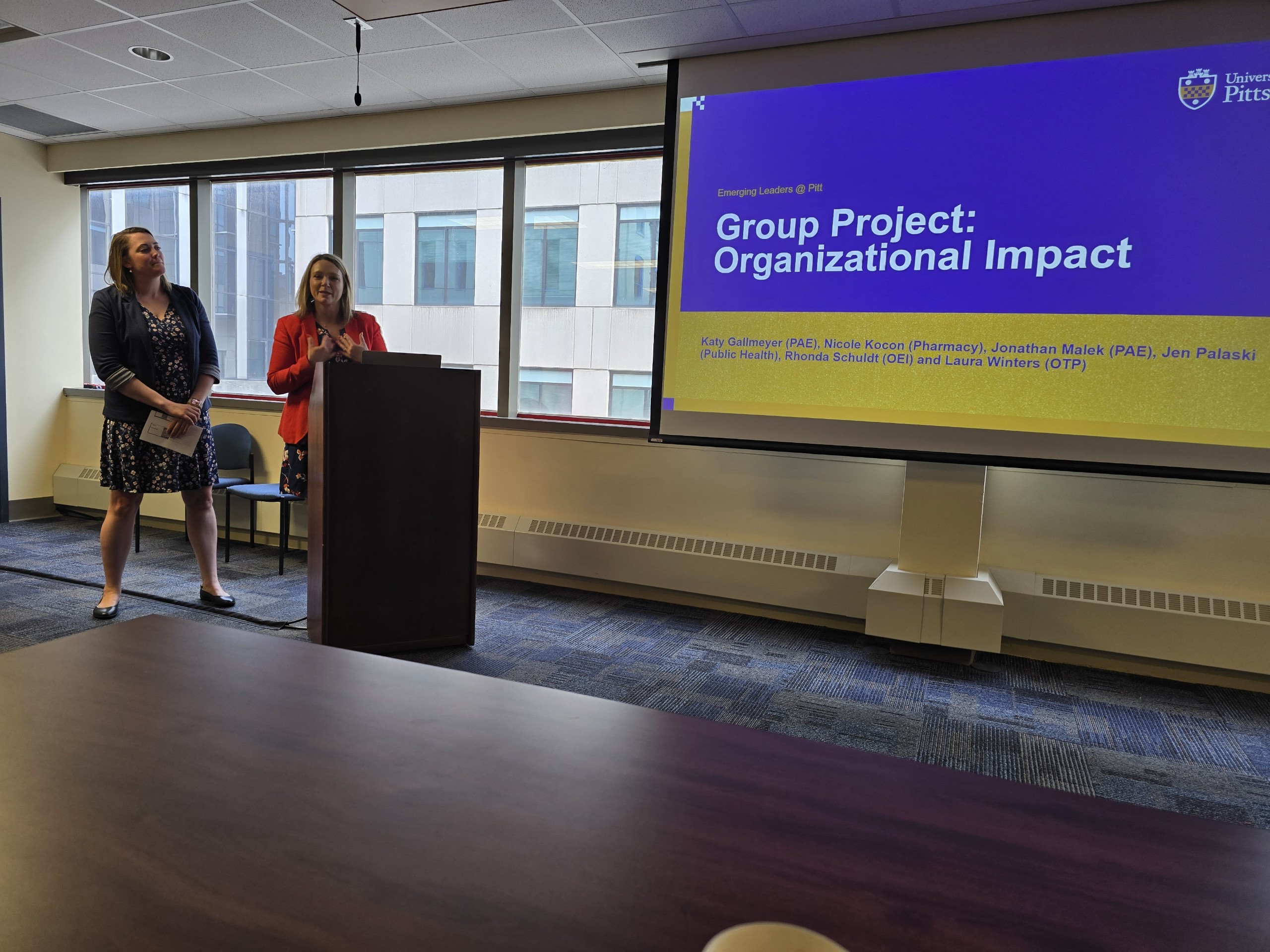 Woman in orange jacket and woman in black dress presenting a talk on organizational impact