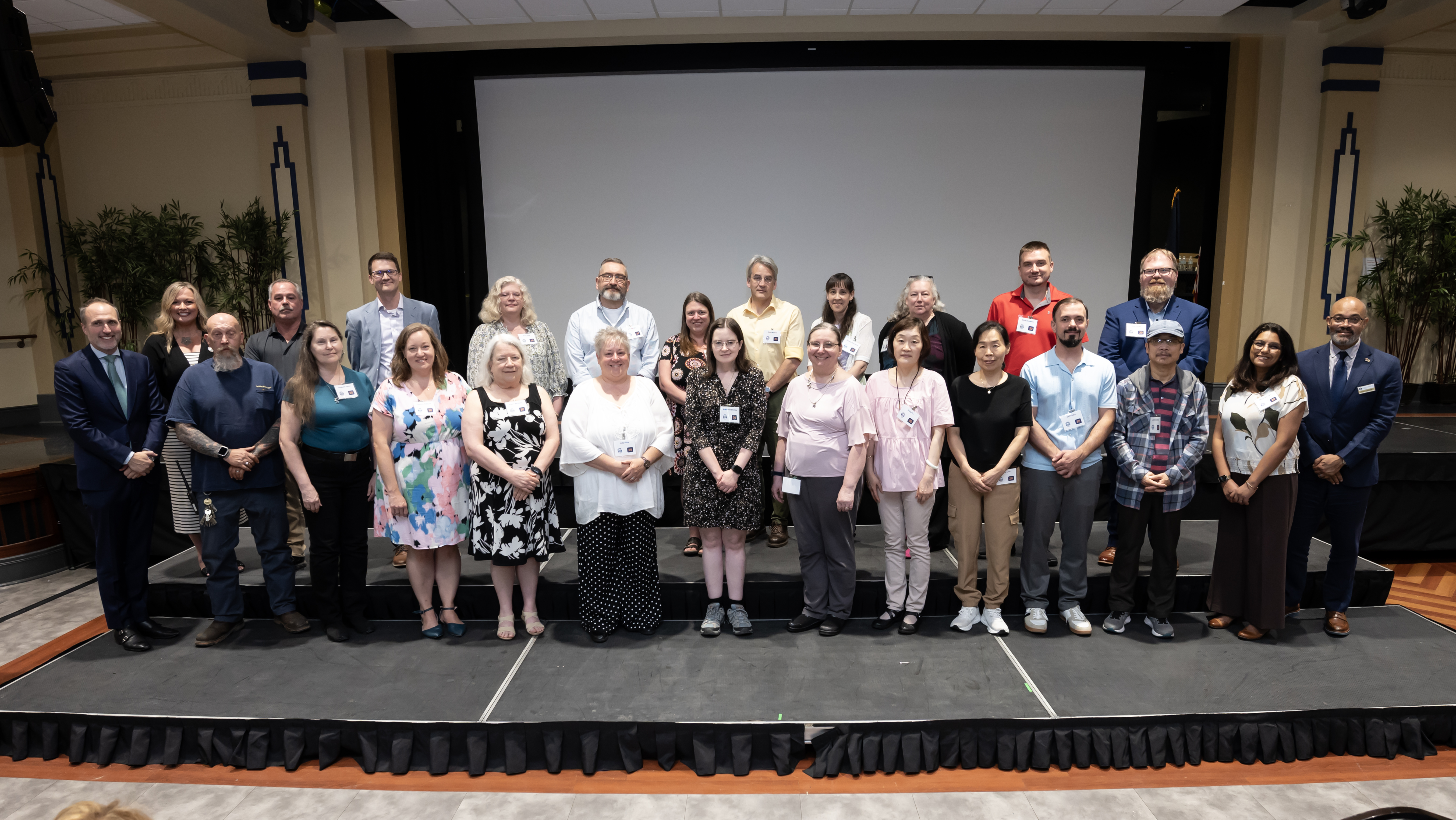 Two rows of Pitt employees standing and smiling while being recognized for their years of service during a ceremony