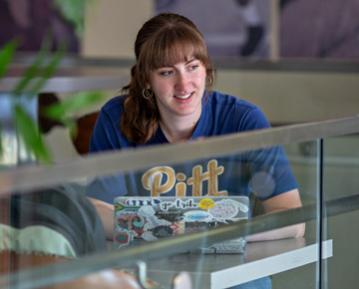 Student on campus on laptop wearing Pitt tshirt