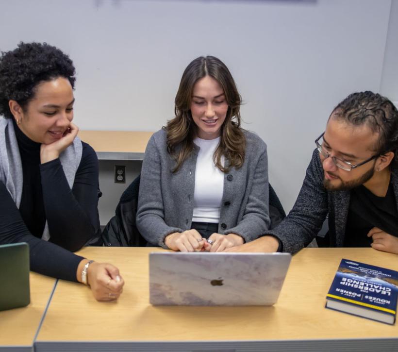 Three HPM students in Public Health building with laptops and book The Leadership Challenge