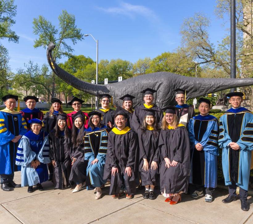 2024 graduates near dinosaur statue outside of Carnegie Music Hall