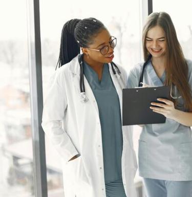 Two women in front of a hospital window discussing a chart.