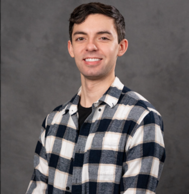 Man with brown hair in a checkered shirt smiling.