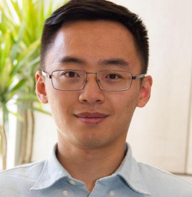 Headshot of a man wearing glasses and a collared shirt in front of a plant.