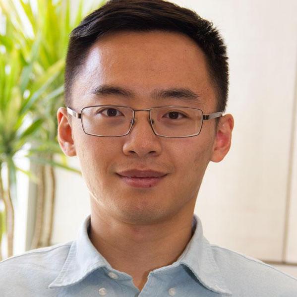 Headshot of a man wearing glasses and a collared shirt in front of a plant.